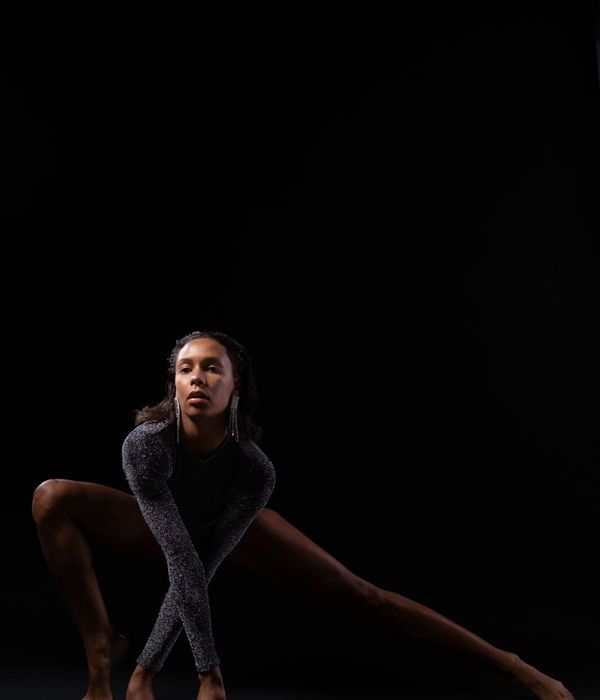 Woman in a dynamic yoga pose against a dark background with fuchsia light.